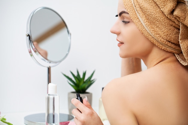 Cute woman in bathroom doing cosmetic procedure for facial skin care