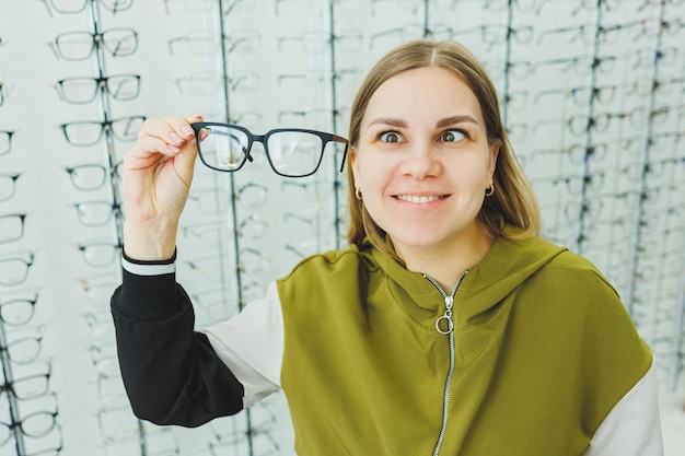 A cute woman chooses glasses in an ophthalmic store A woman buys glasses A woman on the background of shop windows with different models of glasses