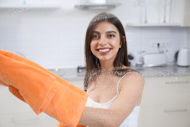 Милая женщина моет окно оранжевой тряпкой