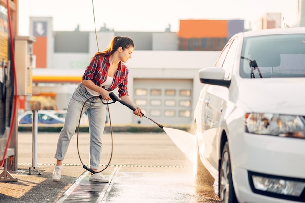 Милая женщина чистит автомобильные колеса с помощью водяного пистолета под высоким давлением.