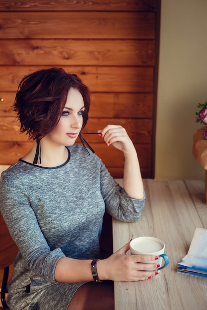 Cute woman drinking coffee in white cup in cafe on city. Fall casual fashion, elegant everyday look. Plus size model.