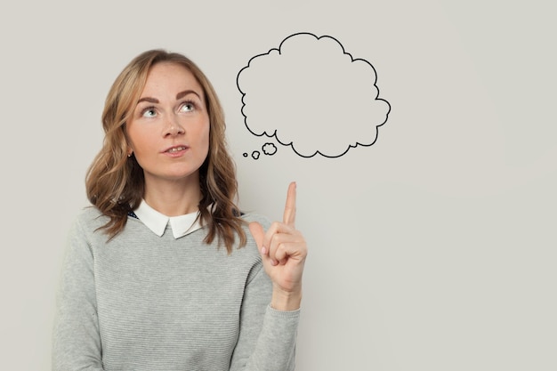 cute woman in gray sweater pointing to think cloud on grey background