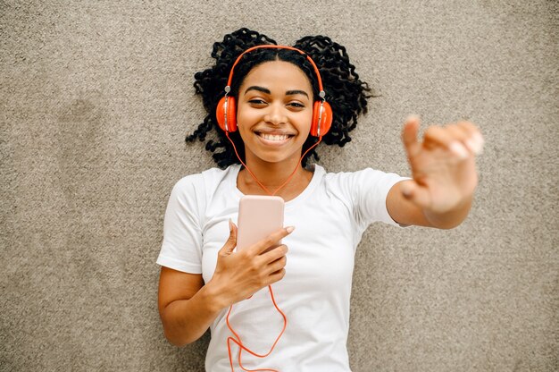 Cute woman in headphones lying on the floor and listen to music, top view. Pretty lady in earphones relax in the room, female sound lover resting