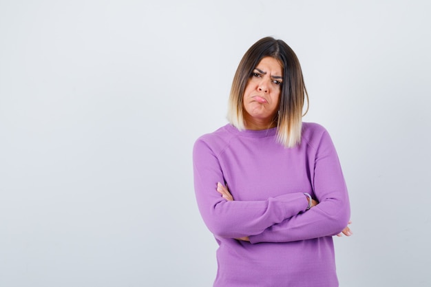 Cute woman holding arms folded, curving lower lip in purple sweater and looking dismal. front view.