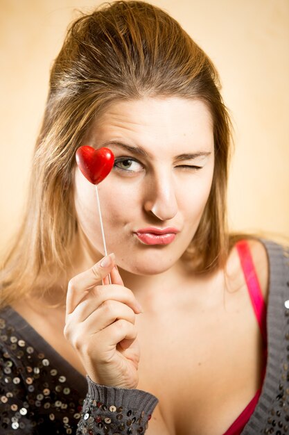 Cute woman holding decorative red heart and looking at camera