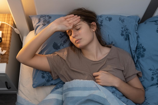 Cute woman lying in bed holding hand on head and suffer from heat temperature Girl feeling bad