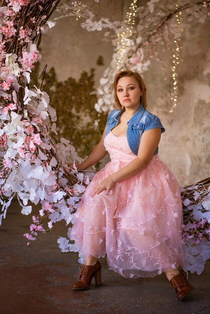 Cute woman in pink dress in studio with flowers