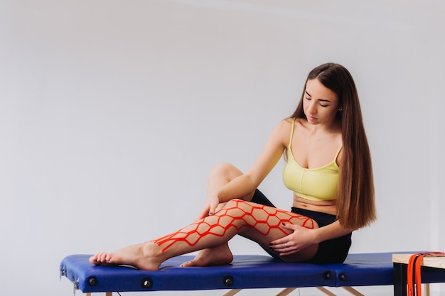 Donna carina posizionando il nastro elastico kinesio su ginocchio e gamba.