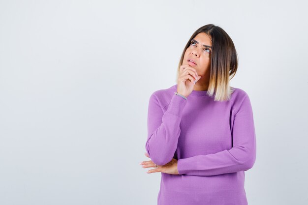 Cute woman in purple sweater with hand on chin, looking up and looking pensive , front view.