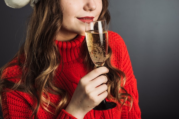 Donna carina con cappello di babbo natale e maglione rosso celebra il natale e beve champagne da un bicchiere