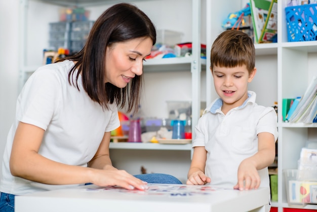 Cute woman speech therapist teaches child to pronounce words sounds and letters correctly in office