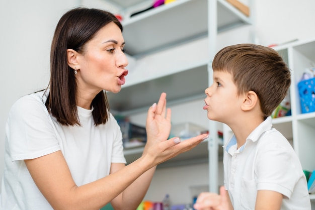 Foto una donna carina logopedista insegna al bambino a pronunciare correttamente parole, suoni e lettere in ufficio