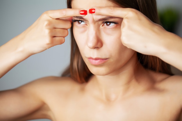 Cute woman squeezed a pimple on her face in front of a mirror
in the bathroom