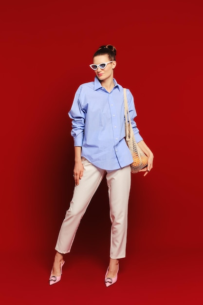 Cute woman in sunglasses with oranges in reusable string bag over the shoulder