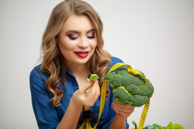 果物と野菜の背景にブロッコリーを保持しているテーブルでかわいい女性