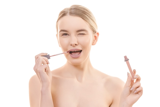 The cute woman using a lip gloss on the white background