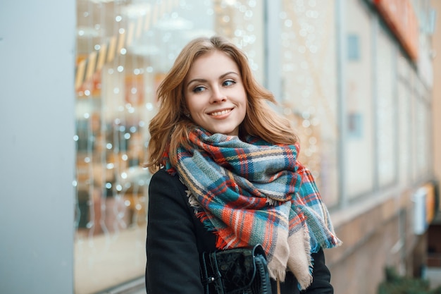 Cute woman in warm clothes with store with lights behind her