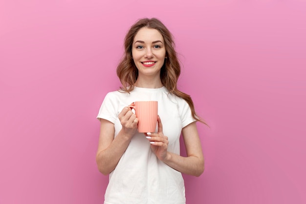 Photo cute woman in white tshirt holding cup of coffee and smiling on pink background