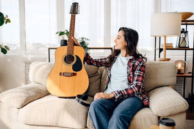 自宅でギターを持つかわいい女性、ヘッドフォン。楽器を持つかわいい女性が部屋でリラックスし、女性の音楽愛好家が休む
