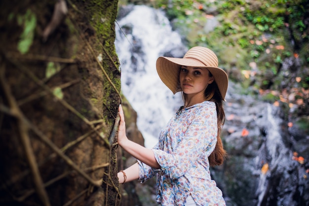 Cute woman with a hat posing by the forest waterfalls