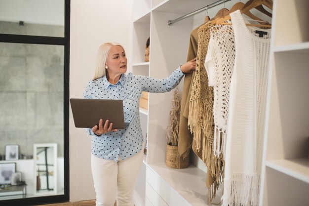 Cute woman with laptop choosing clothes