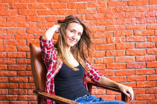 Cute woman with long legs sitting in the armchair behind a brick wall.