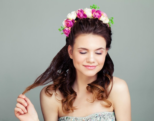 Donna carina con acconciatura perfetta e trucco su sfondo grigio giovane modello femminile con fiori nei capelli