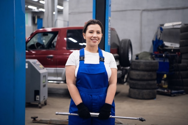 Cute woman in working overalls holds a wrench in her hands and smilimg