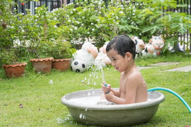 かわいいアジアの少年、泡立つ泡で屋外で浴槽で遊んでいる。