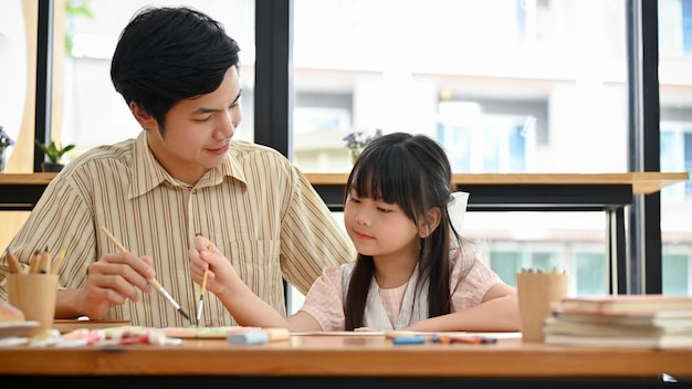 A cute young Asian girl having fun while painting a watercolor with her art teacher