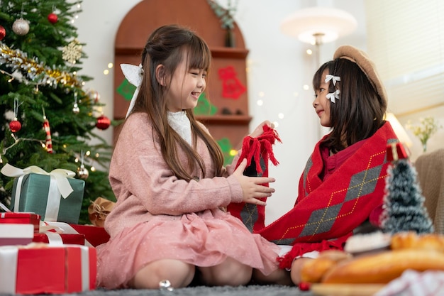 귀여운 아시아 소녀가 여동생에게 크리스마스 선물로 편안한 스카프를 주고 있습니다.