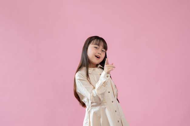 A cute young asian girl is pointing her finger at the camera an isolated pink background