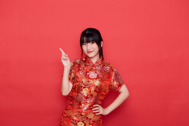 Cute young Asian woman wear cheongsam Pointing to empty for Chinese new year concept on a red