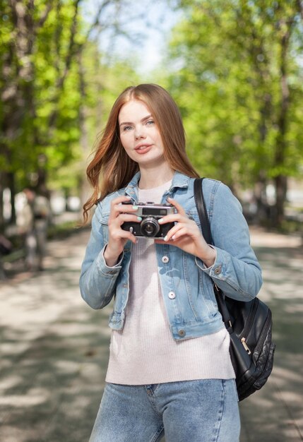 写真 市内のレトロなカメラとデニム ジャケットを着たかわいい若い魅力的な女性観光客