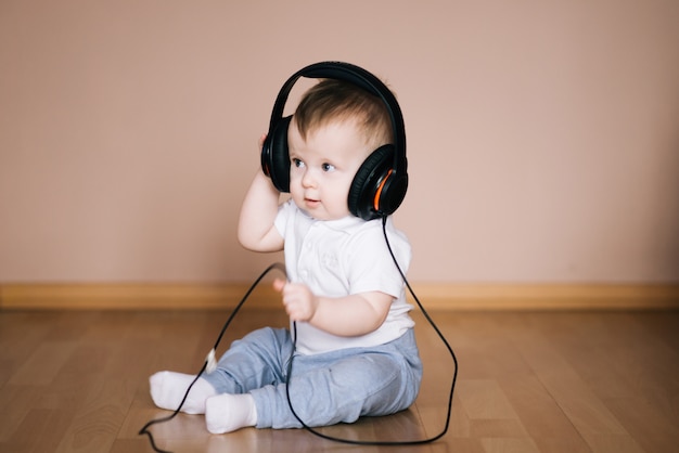 Cute young baby sitting on the floor at home playing with headphones listening to music