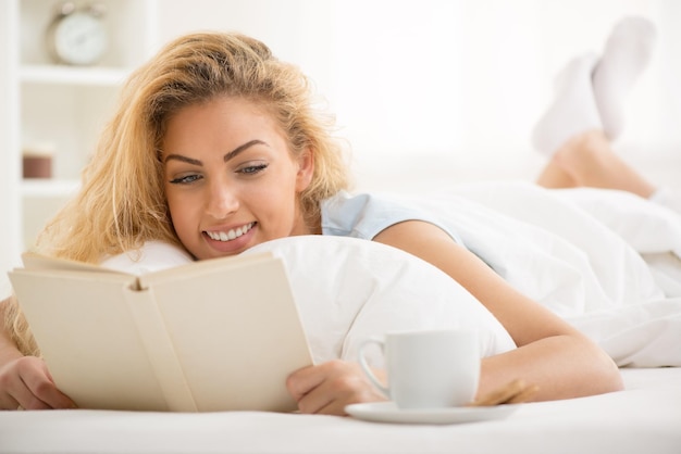 Cute young beautiful woman reading book in the bed