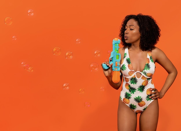 Cute young black woman in swimwear blowing water gun copy space