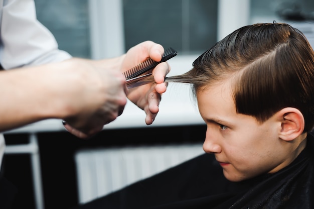 Giovane ragazzo sveglio che ottiene un taglio di capelli in parrucchiere.