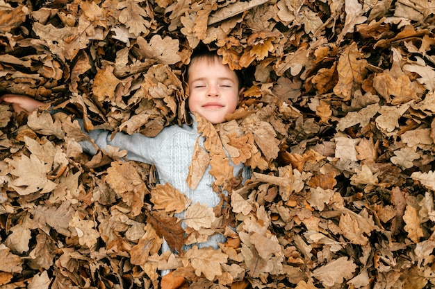 A cute young boy lying in leaves