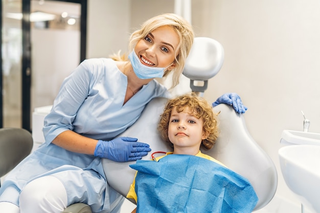 Симпатичный молодой мальчик, посещающий стоматолога, его зубы проверяет стоматолог-женщина в стоматологическом кабинете.