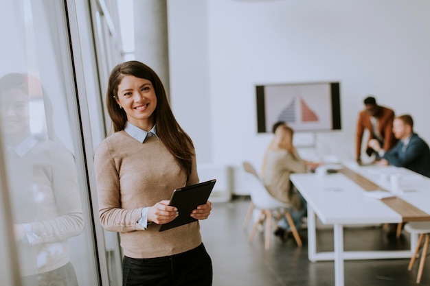 Cute young business woman standing in the office and using digital tablet in front of her team