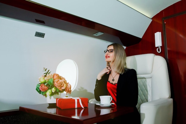 Cute young businesswoman with gift flying in luxury private jet