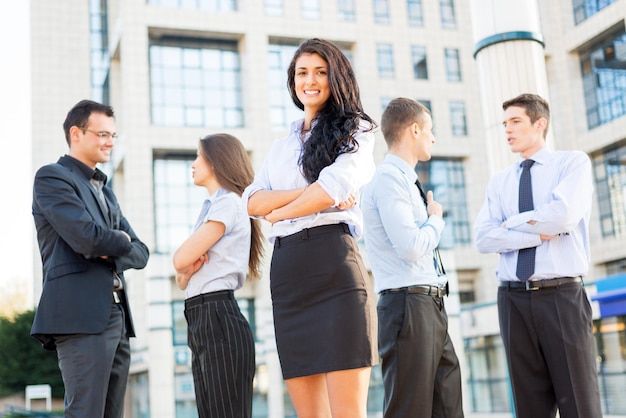 Cute young businesswoman with her team young business people standing in front of office building.