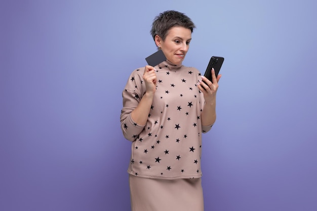 Cute young caucasian darkhaired lady in a skirt and blouse with a short haircut pays for shopping