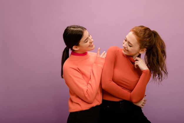 Cute young caucasian girls brunette and redhead in casual clothes look at each other on purple background People emotions lifestyle and fashion concept