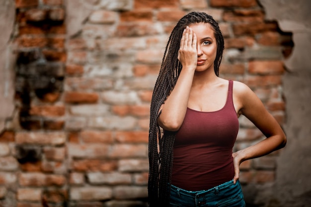 Cute young caucasian woman with long afro braided hair is posing against a brick wall.