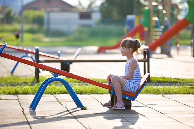 Cute young child girl outdoors on see-saw swing on sunny summer day.