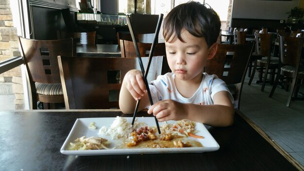 Photo cute young chinese and caucasian boy learning to use chopsticks at restaurant