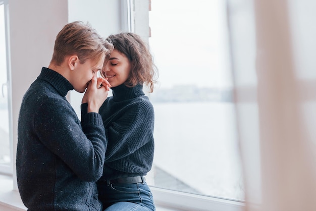 Cute young couple embracing each other indoors near the window.