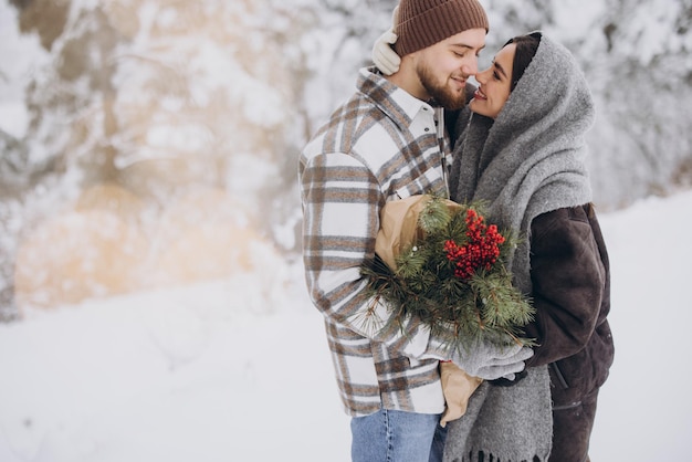 Cute young couple in love with pine bouquet spending time on valentine's day in snowy winter forest